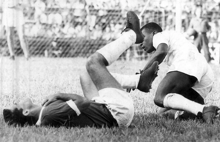 Trombada entre Rinaldo que caiu no chão com as mãos no peito e o Rei Pelé, que levanta lentamente após o choque