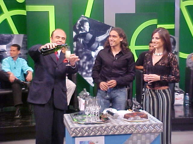 Cacá serve uma taça de champanhe para Sorín, com Daniela Freitas ao seu lado. Atrás, aparecem Adriano e Anderson (parcialmente encoberto por Daniela)