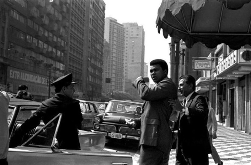 Muhammad Ali em 1971 na Avenida São João, no centro de São Paulo. O motorista do Galaxie conduziu o então pugilista durante o período em que ficou na capital paulista. Ele ficou hospedado no Hotel São Raphael, no centro da cidade. Será que o motorista do carro de trás, um Aero Willys, acreditou que o mito do boxe estava à sua frente? 
