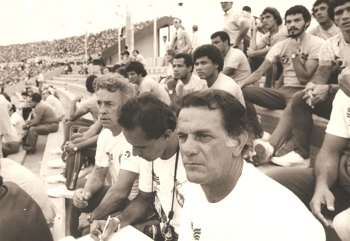 A comissão técnica e os jogadores acompanhando um jogo durante a preparação brasileira para a Copa da Espanha. Na primeira fileira, da esquerda para a direita: Valdir Joaquim de Moraes, Moraci Santana e Telê Santana. Atrás estão Tita, Luisinho e Edvaldo. Na terceira fileira, Getúlio, Sócrates e Zé Sérgio. Mais acima, Oscar e Batista. Foto: arquivo de Valdir Joaquim de Moraes