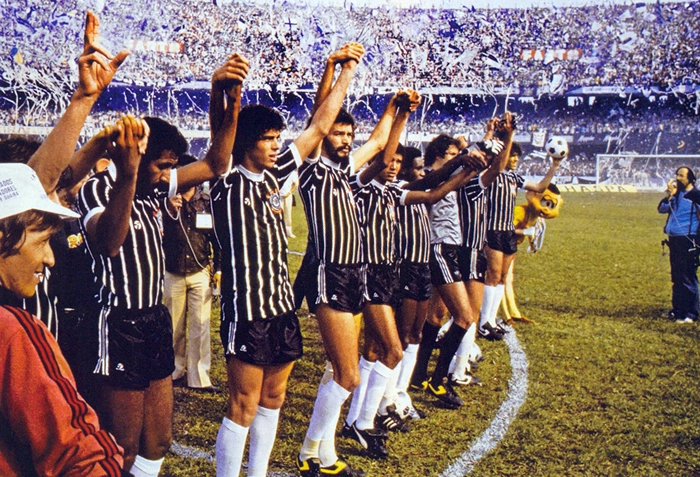 Atletas do Corinthians aparecem saudando sua torcida antes do jogo diante do São Paulo, vencido pelo Alvinegro por 3 a 1. A partida foi realizada no estádio do Morumbi, no dia 12 de dezembro de 1982. Na imagem, da esquerda para a direita, aparecem Mauro, Casagrande, Sócrates, Alfinete, Ataliba, Solito e o último jogador é Paulinho. À frente deles, empunhando o microfone da Jovem Pan, está repórter Wanderley Nogueira. Foto: Placar
