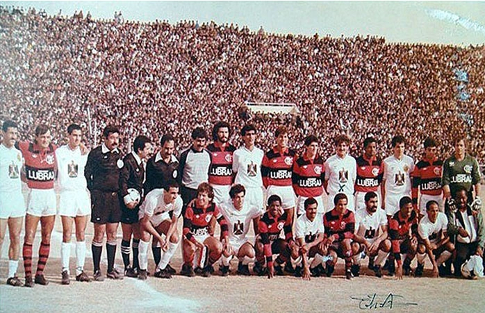 Estádio iraquiano lotado para ver o Flamengo de 1986, com Sócrates e Zico. Na foto, a equipe rubro-negra está junto ao time do Iraque. Em pé, da esquerda para a direita, apenas os flamenguistas: Leandro, Sócrates, Mozer, Jorginho, Andrade, Bebeto e Cantarelli. Agachados: Zico, Adílio, Adalberto e Chiquinho. Foto enviada por Gilvannewton Souza