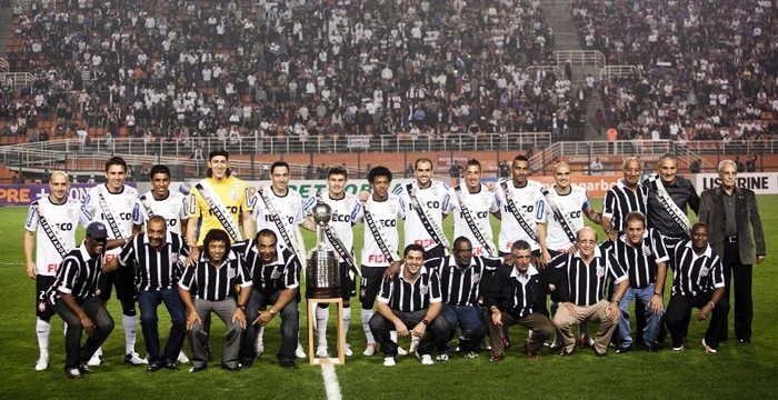 Na imagem, os jogadores que ganharam a Libertadores de 2012 aparecem em pé, enquanto os atletas que triunfaram no Paulista de 77 estão agachados. Foi a entrega da faixa para os jogadores campeões do torneio continental, em 11 de julho de 2012, no Pacaembu. Em pé, da esquerda para a direita: Alessandro, Paulo André, Paulinho, Cássio, Chicão, Alex, Romarinho, Danilo, Ralf, Elton, Fábio Santos, Tobias, Tite e José Teixeira. Agachados: Zé Maria é o primeiro, o segundo é Basílio, Romeu Cambalhota aparece em terceiro, Geraldão em quarto, Ivan é o sexto, Zé Eduardo o sétimo, o oitavo é Lance e o último é Wladimir. Foto: UOL