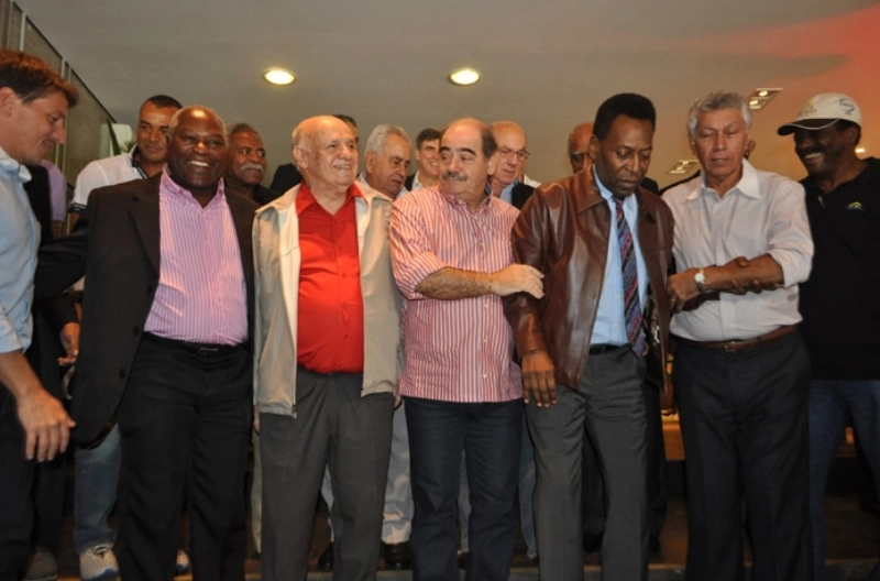 Pelé, recuperando-se de cirurgia no quadril, é amparado por Rivellino e Clodoaldo no almoço dos campeões mundiais no Espaço Unyco, no Morumbi, em 25 de abril de 2013. Os três primeiros, da esquerda para a direita, são Juninho Paulista, Edu e Pepe e o último é Zé Maria. Atrás estão Cafu, Coutinho, Zito, Dino Sani e Mengálvio. Foto: Marcos Júnior Micheletti/Portal Terceiro Tempo