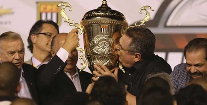  Em 19 de maio de 2013, Mário Gobbi, presidente do Corinthians, beija a taça de campeão paulista ao lado de José Maria Marin, presidente da CBF, à esquerda, no centro o então presidente da Ferderação Paulista de Futebol, Marco Polo Del Nero, e na extrema direita, Reinaldo Carneiro Bastos. Crédito da foto: UOL. 