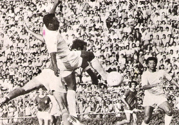 Enquanto Pelé disputa a posse da bola com o adversário, Alcindo, seu colega de ataque, observa o lance. Foto: Reprodução/Revista do Santos