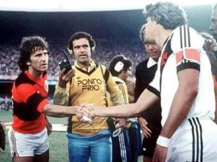 Zico cumprimenta Roberto Dinamite antes de clássico entre Flamengo e Vasco no Maracanã nos anos 80. O repórter, entre eles, é Kleber Leite e o árbitro, parcialmente encoberto por Roberto Dinamite, é José Roberto Wright
