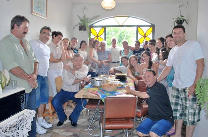Milton Neves, Édson Dino atrás de Milton Neves (de óculos e camiseta listrada), Netto Neves sentado na ponta da mesa e atrás está Lenice Neves (com camiseta verde e branca), reunidos com a Família Magnoni e Neves