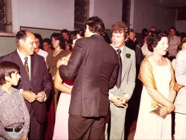 Familiares e amigos se reuniram no Clube Recreativo de Muzambinho para o casamento de Milton e Lenice, em 6 de janeiro de 1978. À esquerda, sorrindo, está o tio Zezinho Neves, de Ribeirão Preto. Milton está de costas, sendo cumprimentado por sua cunhada Cláudia. Regis Policarpo, de terno cinza, observa os dois, e a moça à direita, com a bolsa dourada na mão, é Maria Célia, esposa de Armando Santos, primo de Milton Neves
