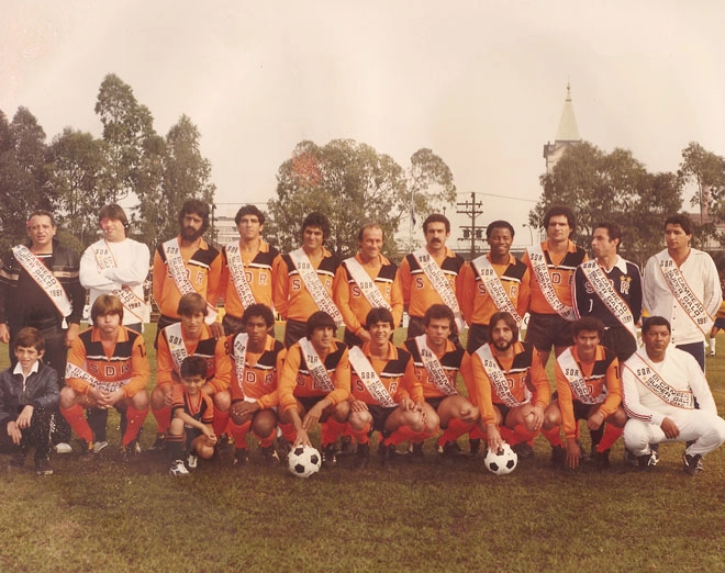A equipe que venceu o Desafio ao Galo em 1980 e 1981 posa para a foto com a faixa de campeã. O segundo em pé, da esquerda para a direita é Écio Pasca e o sexto agachado é Manfrini