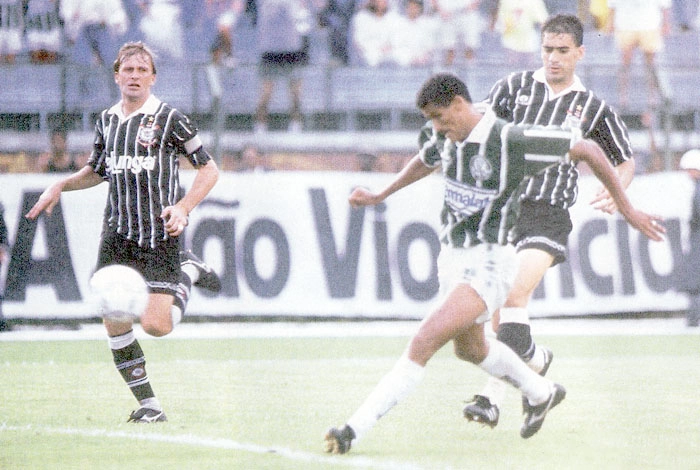 Rivaldo chuta a bola, observado por Henrique, à esquerda, e Gralak, à direita. Imagem: Reprodução
