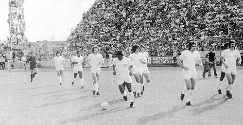 A foto é inédita e mostra a última partida de Pelé em São José do Rio Preto (SP). O Santos FC está entrando em campo e o Rei corre com a bola. Ele está entre dois cabeludos: Brecha (esq) e Zé Carlos (dir). O goleiro Cejas é o primeiro à esquerda, seguido por Clodoaldo. Marinho Peres está em primeiro plano e o bigodudo Vicente é o último. Repare que a torre de iluminação virou arquibancada para a última apresentação do Rei em Rio Preto. Quanto será que foi o ingresso para tal 