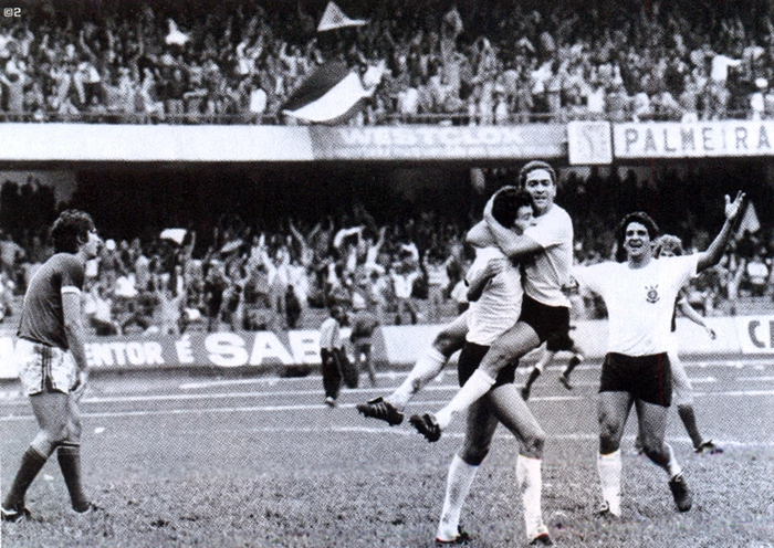 O Timão bateu o Alviverde, em partida realizada em 12 de novembro de 1978, com dois gols de Sócrates e um de Vaguinho. Na imagem, Sócrates celebra um de seus tentos abraçado com Palhinha. Vaguinho corre para comemorar com seus companheiros, tendo o lateral palmeirense Pedrinho Vicençote atrás. À esquerda da imagem, o zagueiro Marinho Peres lamenta o gol sofrido. Foto: Placar
