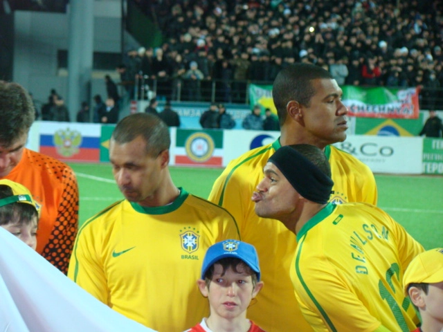 Denílson Show tentando dar um beijo no ex-lateral Zé Maria, enquanto Zetti aparece à esquerda e Júnior Baiano ao fundo. A foto foi tirada em março de 2011, quando os veteranos da Seleção Brasileira enfrentaram em combinado da Chechênia
