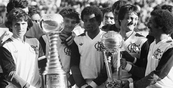 Jogadores do Flamengo comemoram título mundial sobre o Liverpool em 1981. Da esquerda para a direita: Zico, Raul Plasmann (encoberto), Tita, Andrade, Leandro e Júnior. Sorrindo, no fundo, o jornalista Kléber Leite. Crédito da foto: Agência O Globo, via Portal UOL. 