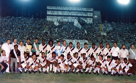 Elenco do Vasco da Gama reunido em S&atilde;o Janu&aacute;rio com a faixa no peito referente &agrave; conquista do t&iacute;tulo brasileiro de 1989. Em p&eacute; est&atilde;o membro da comiss&atilde;o t&eacute;cnica, Ademar Braga, o t&eacute;cnico Nelsinho Rosa, Ac&aacute;cio, M&aacute;rcio, Marco Aur&eacute;lio, Qui&ntilde;onez, R&eacute;gis, dois jogadores n&atilde;o identificados, Oliveira, Ayupe, Andrade, C&eacute;lio Silva, Luiz Carlos Winck, dois dirigentes e Eurico Miranda. Agachados est&atilde;o outro membro da comiss&atilde;o t&eacute;cnica n&atilde;o identificado, Alcir Portela, Z&eacute; do Carmo, Tita, Vivinho, jogador n&atilde;o identificado, Sorato, outro jogador n&atilde;o identificado, Boiadeiro, Mazinho, Sony Anderson, Tato, Bismarck, William e C&aacute;ssio