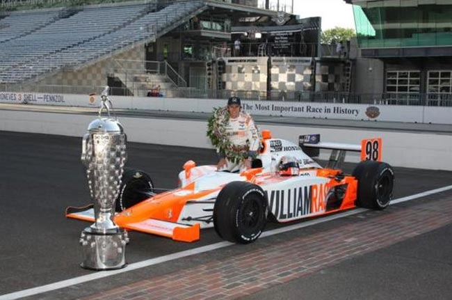 Wheldon com seu vitorioso carro da equipe Bryan Herta com o qual conquistou as 500 Milhas de Indianápolis em 2011, e o troféu da prova. Foto: Divulgação