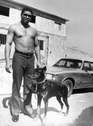 Em plena forma, em 1987, com Panter, seu doberman, em frente à sua casa, em construção. Estacionado, o Opala Diplomata do ex-boxeador. Foto: UOL