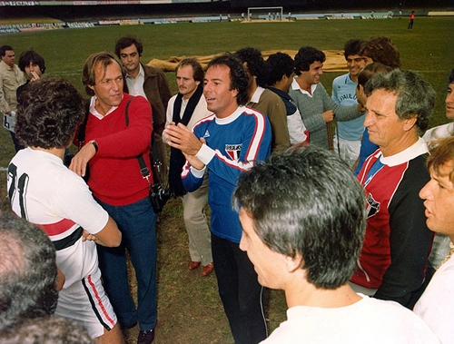 Julio Iglesias vestiu nesse dia a camisa 1 de Waldir Peres. De costas, vemos a cabe&ccedil;a e o perfil do ex-volante Almir. Ele &eacute; seguido, no sentido anti-hor&aacute;rio, por Marinho Chagas, de corrente. Poy est&aacute; com o agasalho tricolor. No fundo, Barbirotto aparece de camisa azul, sorrindo. Do lado esquerdo dele est&aacute; o zagueiro Oscar. 