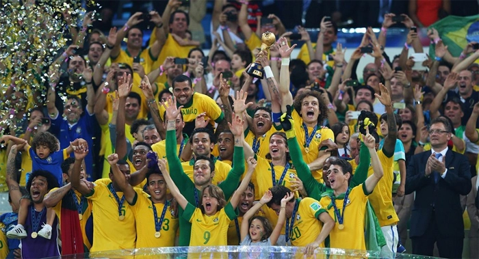 Da esquerda para a direita e de baixo para cima, na primeira fila: Marcelo, Hulk, Fernando, Jean, Júlio César, Neymar, Bernard e Oscar. Na segunda fila: Jô, Fred, Filipe Luiz, Jefferson, Luiz Gustavo e Jérôme Valcke batendo palmas. Na terceira fila: Carlos Alberto Parreira, Réver, Daniel Alves (que salta sobre Réver), Thiago Silva com a taça, David Luiz e José Maria Marin (parcialmente encoberto). Foto: Fifa