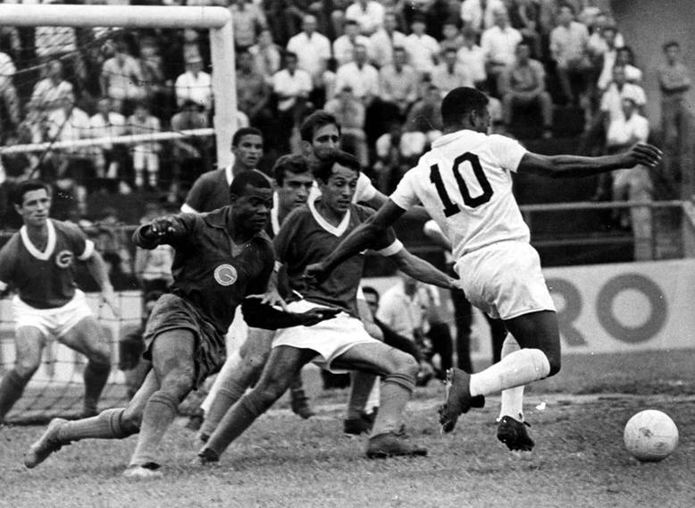 Nos anos 60, durante um Santos e Guarani, Pelé faz mais uma de suas jogadas geniais. Caravetti (só com o rosto aparecendo), Milton e o goleiro Dimas tentam abafar o Rei no desespero. O santista Toninho Guerreiro (encoberto pelos defensores) espera a conclusão da jogada enquanto Tarciso (ex-Palmeiras - em frente à trave) e o lateral Diogo observam o lance. Foto histórica e característica do maior jogador da história do futebol.