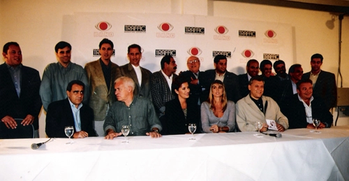 Em foto de Marcos Mendes, durante apresenta&ccedil;&atilde;o da equipe esportiva da Bandeirantes em 1999. Sentados: Oliveira Andrade, Silvio Luiz, Silvia Vinhas, Hort&ecirc;ncia, Milton Neves e Luciano do Valle. Em p&eacute;: Eduardo Vaz, Mauro Beting, Nivaldo Prieto, Rivellino, Orlando Duarte, Antonio P&eacute;trin, Luis Cear&aacute;, Fernando Fernandes, Oswaldo Paschoal, Alexandre Santos e M&aacute;rcio de Castro
