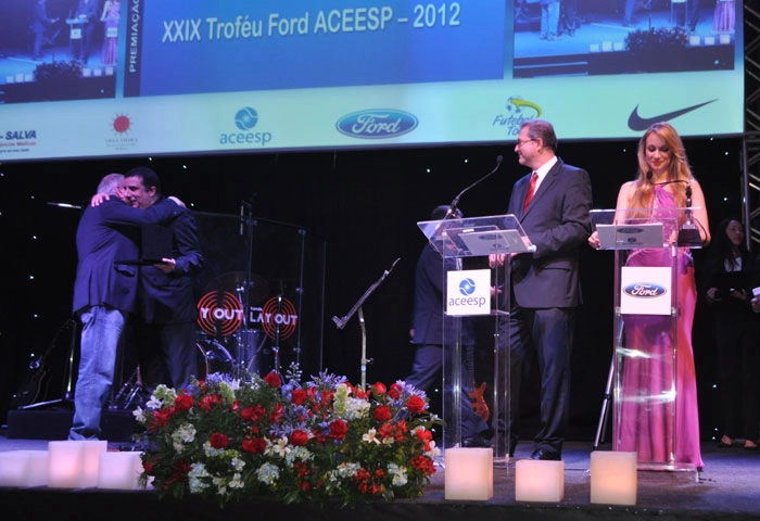 No Pr&ecirc;mio da ACEESP de 2012, realizado no Esporte Clube S&iacute;rio, grandes nomes da m&iacute;dia esportiva marcaram presen&ccedil;a: no palco, Luciano do Valle. prestes a ser homenageado, cumprimenta Oct&aacute;vio Muniz, observados por Jo&atilde;o Palomino e Andressa Lopes